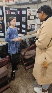 Alexia Riche listens intently to a presentation about the Acadian flag, presented by a youth at the 2025 Provincial Heritage Fair